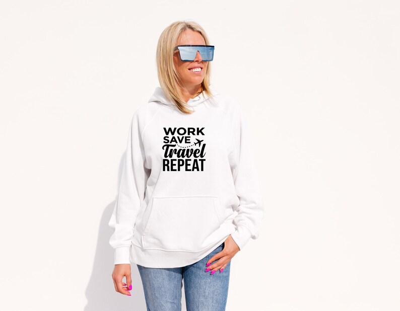 May include: A white hooded sweatshirt with the text "WORK SAVE TRAVEL REPEAT" in black. The sweatshirt has a front pocket and is paired with blue jeans. The image features a person wearing sunglasses.