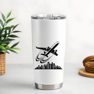 May include: A white travel tumbler with a black and white graphic of an airplane taking off over a city skyline. The tumbler has a silver base and a silver lid. The design is printed on the front of the tumbler.