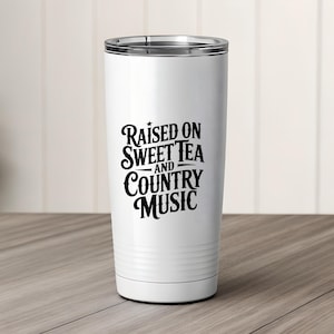 May include: A white insulated tumbler with a silver rim. The tumbler features the black text "Raised on Sweet Tea and Country Music" in a decorative font. The tumbler is designed to keep beverages hot or cold.