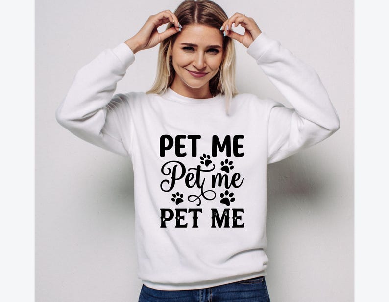 May include: White sweatshirt with the text "PET ME" in a bold, black font, with paw prints and decorative swirls. The sweatshirt is a casual style, suitable for pet lovers.
