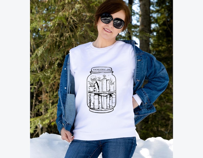 May include: White sweatshirt with a black and white graphic of a jar labeled "KNOWLEDGE JAR" containing books and plants. The sweatshirt is worn with a denim jacket and blue jeans.