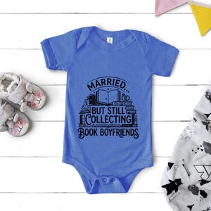 May include: A blue baby onesie with the text "Married... But Still Collecting Book Boyfriends" in black. The onesie is surrounded by baby shoes and a patterned blanket.