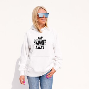 May include: White hoodie with a front pocket and the text "COWBOY TAKE ME AWAY" in black. The graphic includes a horse silhouette above the text. The hoodie is paired with blue jeans.