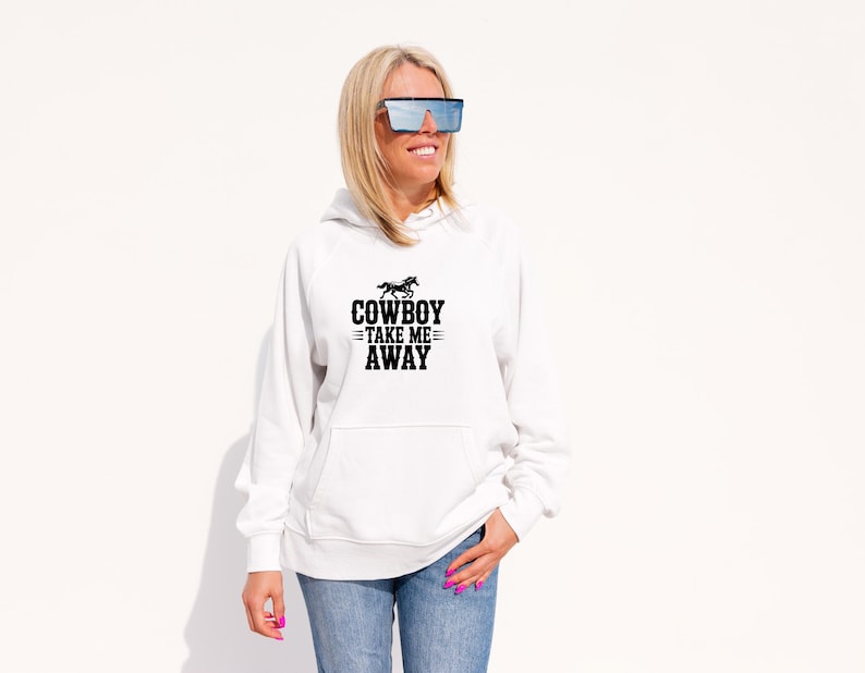 May include: White hoodie with a front pocket and the text "COWBOY TAKE ME AWAY" in black. The graphic includes a horse silhouette above the text. The hoodie is paired with blue jeans.