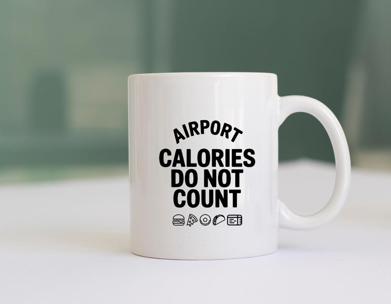 May include: A white ceramic mug with the text "AIRPORT CALORIES DO NOT COUNT" in black. The mug features small food icons below the text, including a burger, pizza slice, donut, taco, and a boarding pass.