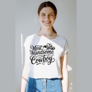 May include: White t-shirt with the text "Most Handsome Cowboy" in a black, stylized font, and a cowboy hat graphic. The shirt is paired with blue denim shorts.