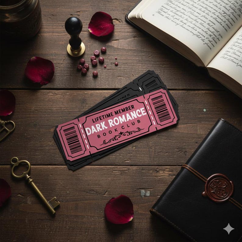 May include: A stack of black tickets with a pink rectangle that reads "LIFETIME MEMBER DARK ROMANCE BOOK CLUB" on a wooden surface. Other items include a book, a key, rose petals, and a journal.