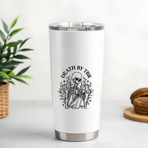 May include: White stainless steel tumbler with a black graphic of a skeleton reading a book, surrounded by foliage, and the text "DEATH BY TBR". The tumbler has a silver base and lid.