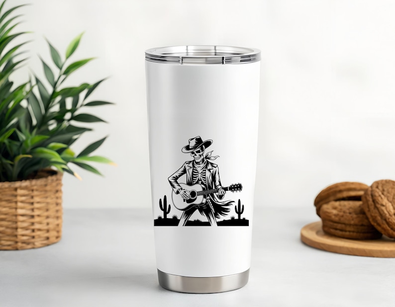 May include: White 20 oz stainless steel tumbler featuring a black and white illustration of a skeleton playing a guitar, wearing a cowboy hat and jacket. The design includes cacti silhouettes. The tumbler has a silver rim and base.