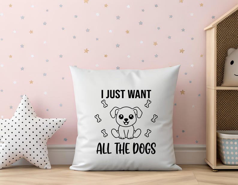 May include: White square pillow with the text "I JUST WANT ALL THE DOGS" and a cartoon dog illustration. The pillow is surrounded by a star-patterned wall and a star-shaped pillow.