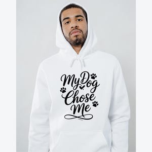 May include: White hooded sweatshirt with the text "My Dog Chose Me" in black script. The design includes paw prints and a heart. The sweatshirt has a drawstring hood and a front pocket.