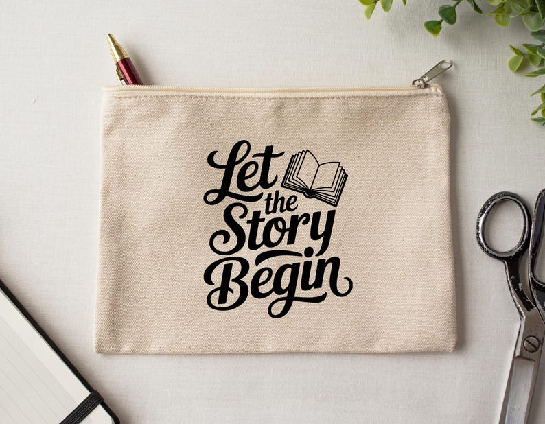 May include: A beige canvas zippered pouch with the text "Let the Story Begin" in black script and a small book illustration. A red and gold pen is in the zipper. The pouch is on a white surface with scissors and greenery.