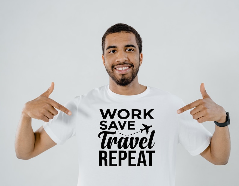 May include: White t-shirt with the text "WORK SAVE TRAVEL REPEAT" in black. A small airplane graphic is above the word "travel". The person in the image is pointing at the shirt.