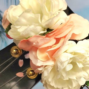 May include: A black hair accessory adorned with clusters of artificial flowers in shades of white and peach. The accessory features gold-colored accents and decorative pink petal details, creating a delicate and feminine aesthetic.