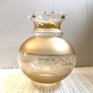 May include: A gold glass lampshade with a white floral design. The lampshade has a ruffled top and a round body.