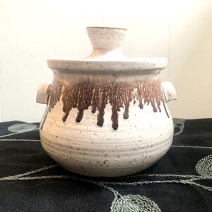 May include: White ceramic crock pot with brown glaze dripping down the sides. The pot has two handles and a lid.