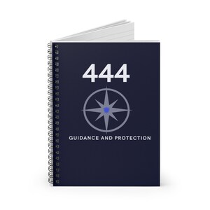 May include: A dark blue spiral notebook with the number 444 printed in white. A gray compass with a blue shield in the center is below the number. The text "Guidance and Protection" is printed below the compass.