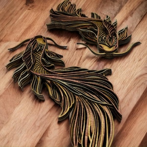 May include: Two layered wooden koi fish sculptures with intricate details. The fish are primarily black and gold, with detailed fins and tails. The sculptures are placed on a wooden surface.