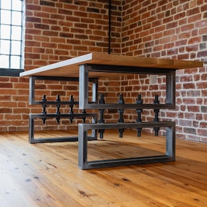 Puede incluir: Mesa de estilo industrial moderno con tapa de madera clara y estructura de acero. La mesa tiene un diseño rectangular con tornillos y tuercas visibles, sobre una pared de ladrillo y suelo de madera. Medidas en cm.