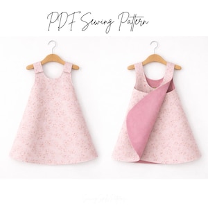 May include: Two pink dresses on wooden hangers. The dresses have a floral pattern and a reversible design. The text "PDF Sewing Pattern" is written in cursive at the top of the image.