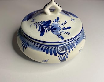 May include: A ceramic sugar bowl with a lid, featuring a cream-coloured base and intricate blue floral patterns. The lid has a handle and is adorned with matching blue designs. The bowl's rim is also decorated with blue brushstrokes, creating a cohesive look.