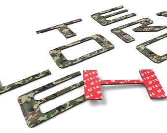 May include: A set of camouflage-patterned letters spelling out "FORD" with adhesive backing. The letters are made of a durable material and are designed to be applied to a vehicle's exterior.