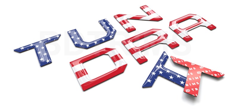 Pu&ograve; includere: Un set di lettere 3D rosse, bianche e blu che compongono la parola "Tundra" con una lettera "TX" pi&ugrave; piccola sotto. Le lettere sono decorate con un motivo di stelle e strisce, che ricorda la bandiera americana.