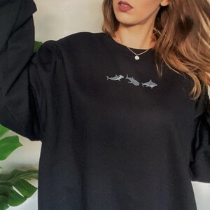 May include: Black sweatshirt with a small embroidered design of three sharks in a row.