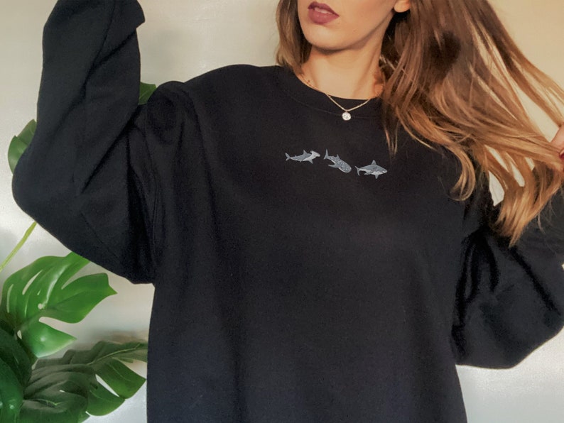 May include: Black sweatshirt with a small embroidered design of three sharks in a row.