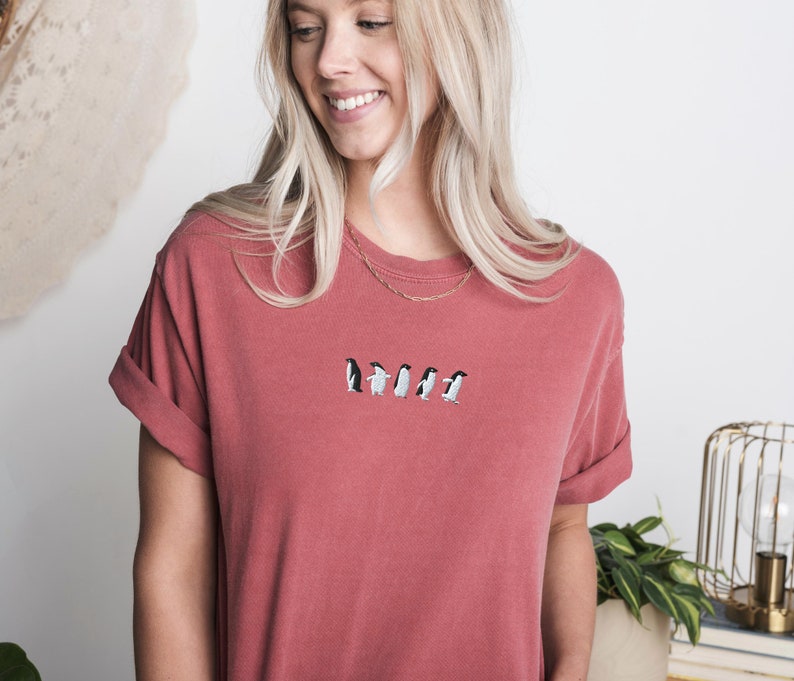 May include: A red t-shirt with a line of embroidered penguins walking across the front.