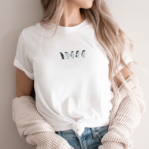 May include: A white t-shirt with a line of embroidered penguins in black and white.