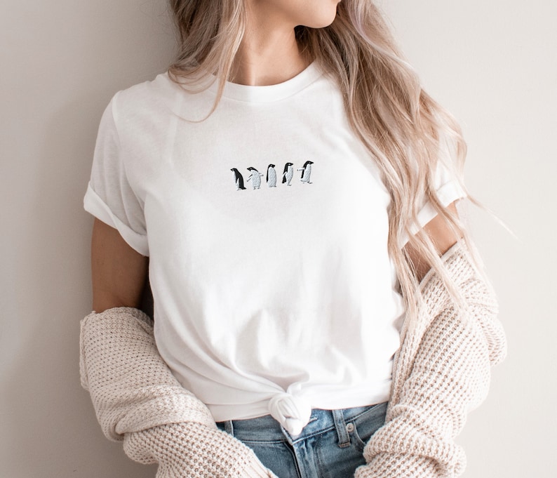 May include: A white t-shirt with a line of embroidered penguins in black and white.