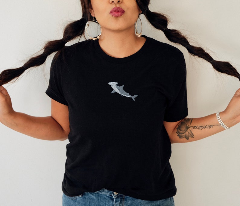 May include: A black t-shirt with a small embroidered hammerhead shark in gray on the front.