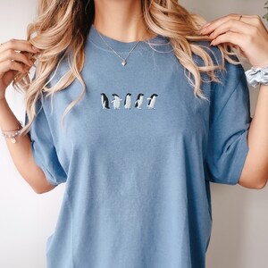 May include: A light blue t-shirt with a line of embroidered penguins in black and white.
