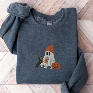 May include: A dark gray sweatshirt with a white ghost wearing a red hat and holding a pumpkin. A black dog is standing next to the ghost.