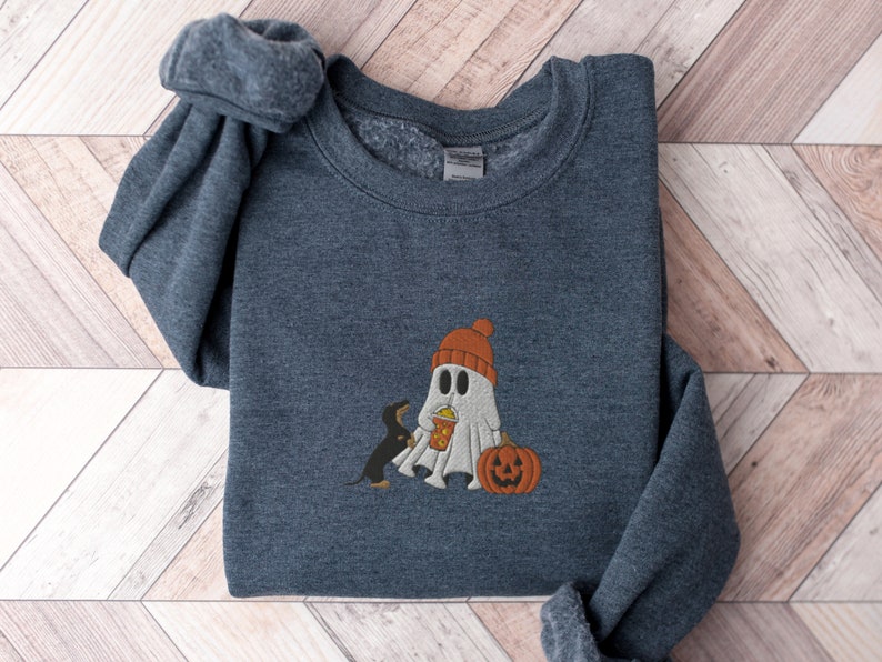 May include: A dark gray sweatshirt with a white ghost wearing a red hat and holding a pumpkin. A black dog is standing next to the ghost.