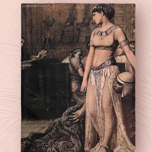 May include: A painting depicting a woman in a white dress and gold jewelry, standing in a room with other people. The woman is holding a white hat in her hand. The painting is titled "GOODSON GALLERY".