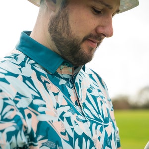 May include: A man wearing a teal and white patterned short-sleeved shirt with a white hat.
