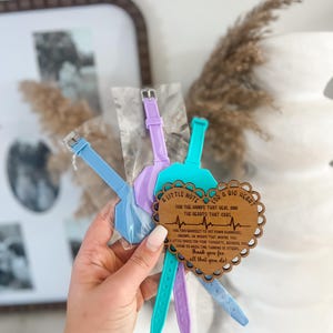 May include: A collection of colorful watch straps in blue, purple, and teal, held together with a wooden heart-shaped tag. The tag has a scalloped edge and includes the text "A Little Note for a Big Heart".