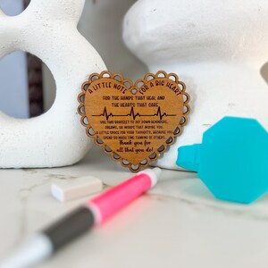 May include: A wooden heart-shaped ornament with a message that reads "A little note for a big heart for the hands that heal and the hearts that care." The ornament features a stylized EKG line and the text "Thank you for all that you do."