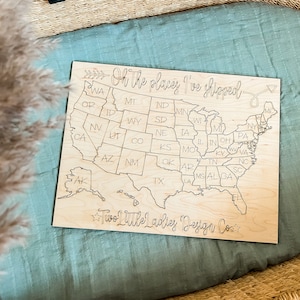 May include: A wooden map of the United States with the text "Oh the places I've shipped" and "Two Little Ladies Design Co."  The map is divided into states with their abbreviations labeled.