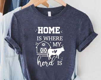 May include: A navy blue t-shirt with a white graphic that says "Home is where my herd is". The graphic includes a barn and a cow with a heart.