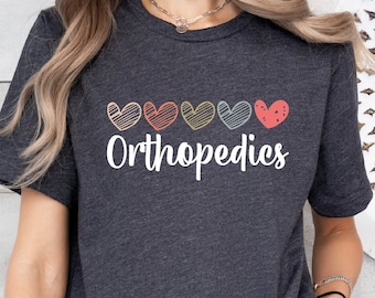 Puede incluir: Una camiseta gris jaspeada oscura con una fila de cinco corazones coloridos y el texto "Orthopedics" impreso en la parte delantera.