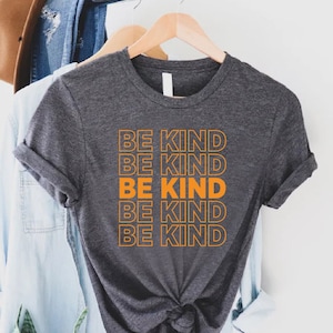May include: A dark gray t-shirt with the phrase "Be Kind" repeated five times in orange outlined text.