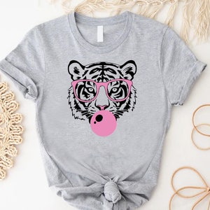 May include: A gray t-shirt with a black and white illustration of a tiger wearing pink glasses and blowing a pink bubble.