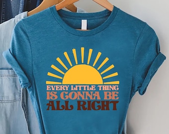 May include: A teal blue t-shirt with a yellow sun graphic and the text "Every little thing is gonna be all right".