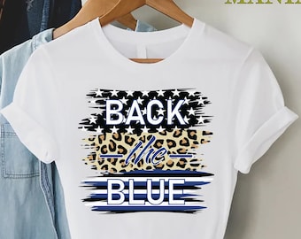 May include: White t-shirt with a graphic design that says "Back the Blue" with a blue and white American flag design, a leopard print design, and a blue line design.