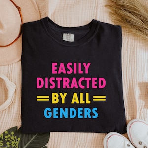 May include: Black t-shirt with the text "Easily Distracted = By All = Genders" in pink, yellow, and blue. The text is centered on the shirt.