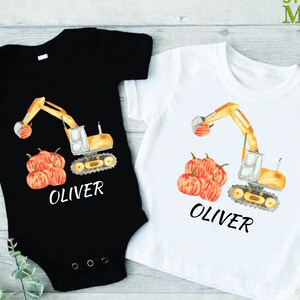 May include: Two white and black short-sleeved shirts with a yellow excavator and orange pumpkins. The shirts are personalized with the name "Oliver".