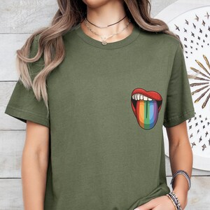 May include: A green t-shirt with a rainbow tongue sticking out of a red mouth graphic on the front. The shirt is being worn by a person with long brown hair.